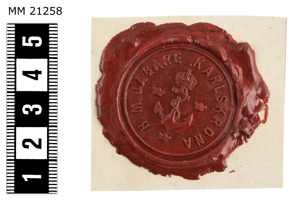 Sigillavtryck av rött lack på papper. I mitten krönt stockankare omgivet av tre kronor. Längs kanten text: "H.M. jagare Karlskrona".