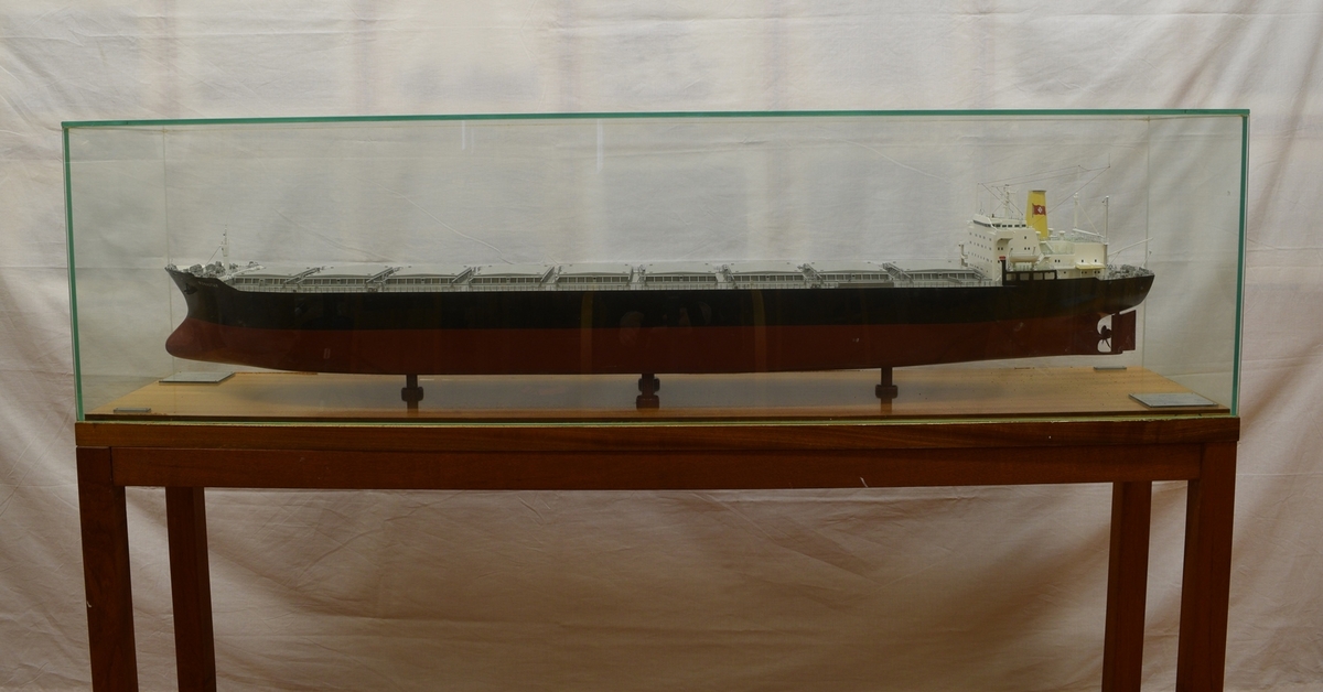 Båtmodell i monter av glass, på stativ av tre.