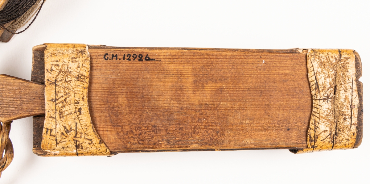 Masklåda med metrev. Lådan märkt 1843, ALS, samt bomärke.
Lådan smal med skjutlock och med näverbeslag.
Vidhängande i kort vidjelänk en liten vinda av trä med reven virad.