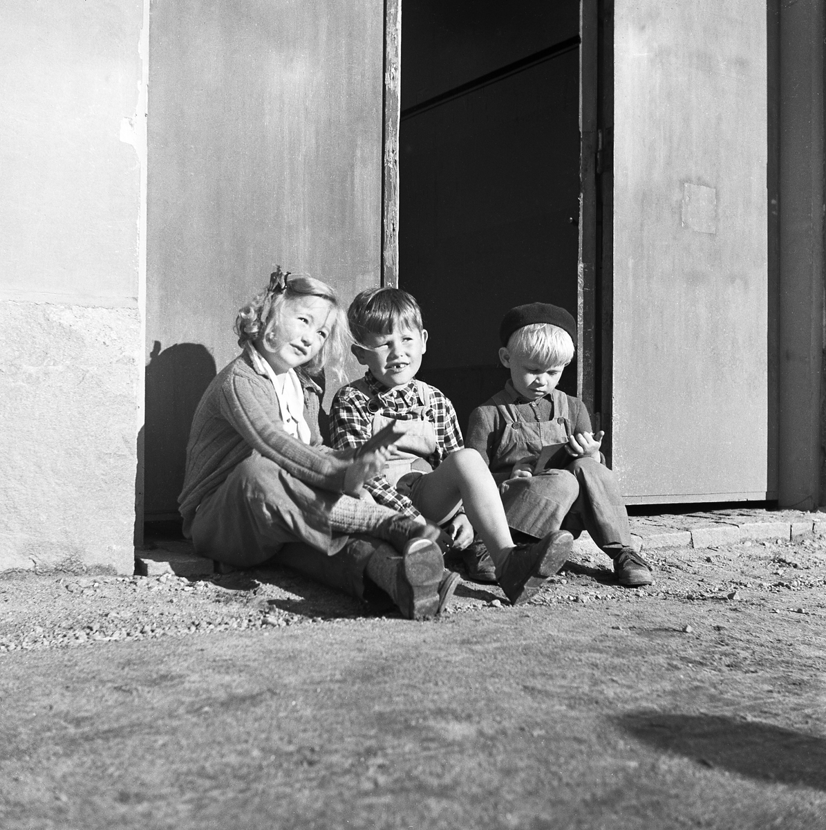 1950-tal. Tre okända barn sitter på en trapp.