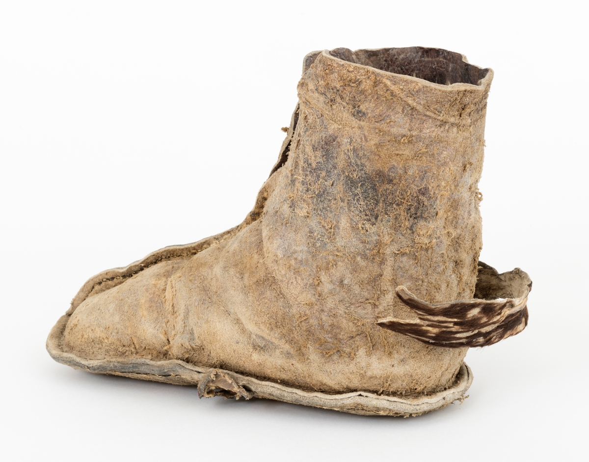 Overlæret er laget av ett skinnstykke. Det har en søm på midten langsetter fra åpningen til tåspissen. Sålene er sydd sammen med overlæret langs kanten. Skoene har hatt to reimer hver til å surre dem fast med. Den ene reima på en av skoene er borte. Reimene på den andre skoen har dyrehåra på. 
Skoene har vært brukt under spilljakt og lurejakt. Giveren kalte dem komager. 
Behandling: Før behandlingen var skoene tørre og harde uten fasong. 
De ble lagt i bløt i vann i 1 uke. Den venstre skoen gikk opp i alle sømmene  ved bløtleggingen. Den er sydd sammen med bektråd. 
Skoene ble behandlet med polyetylenglyol 750 (PEG) gnidd godt inn på yttersiden. Innvendig vasket med 2 % fenol (5 gram fenol til 1/2 l vann)
for å bevare håret. Stoppet i fasong. Skoene vil bli ganske harde etter at de har tørket. 
