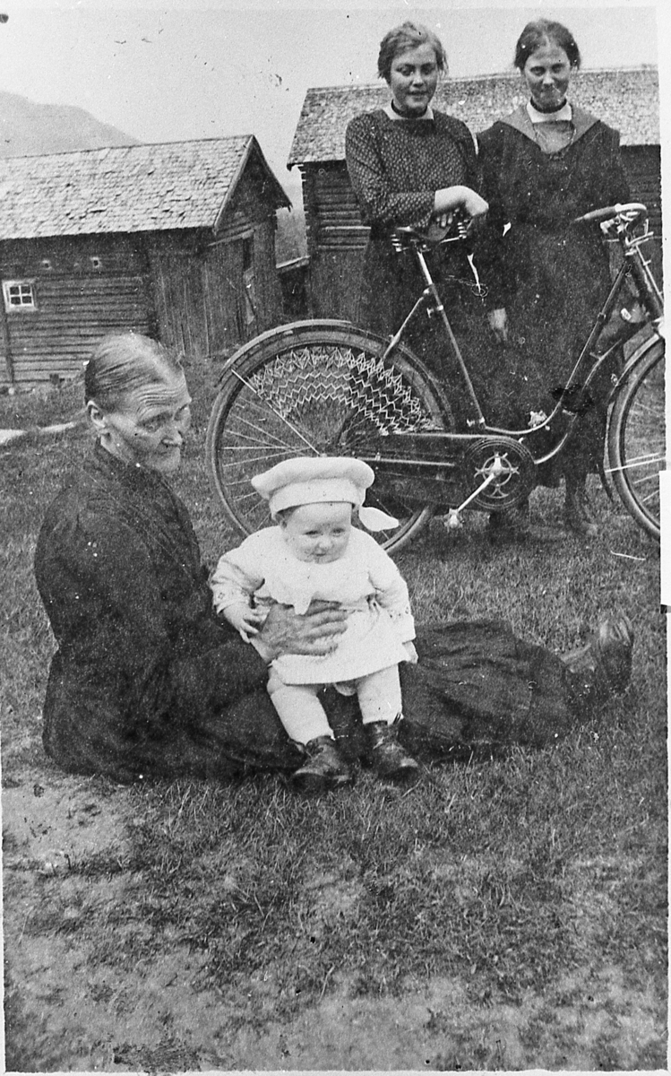 Fra tunet på Nedre Lien i Sigdal, 1919. Kjersti Lien med Nils H. Lien på fanget. Bak med sykkel, fra venstre: Kristi Elverum og Stina Stubberud.