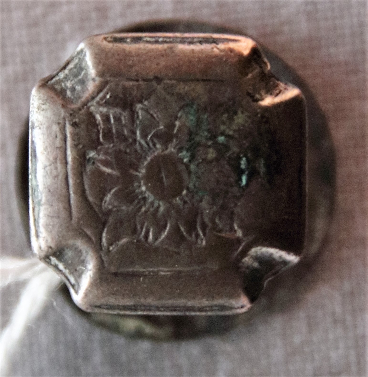 En mindre manschettknapp av silver. Övre delen ett brett likarmat kors (1,3 x 1,3 cm) och i dess mitt en stiliserad graverad ros.