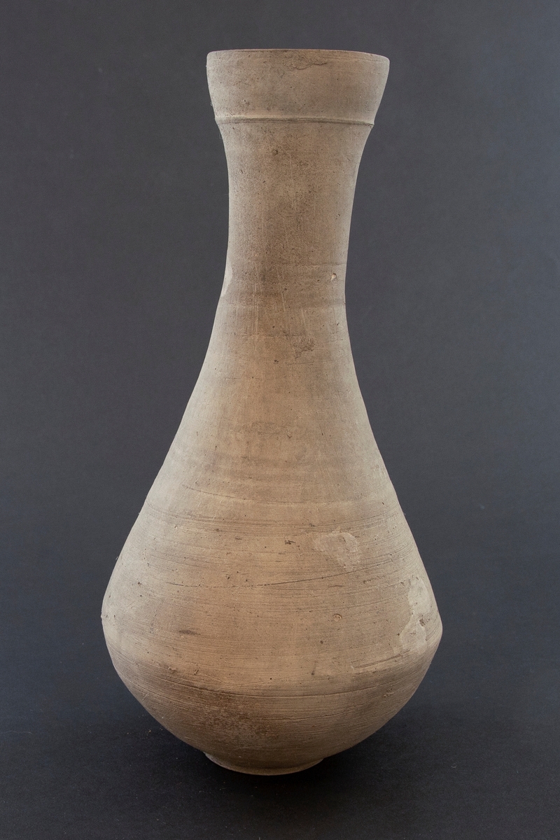 Balusterformet flaske med høy hals og lav fot. Flasken er dreid i gråbrunt leirgods og er uglasert.