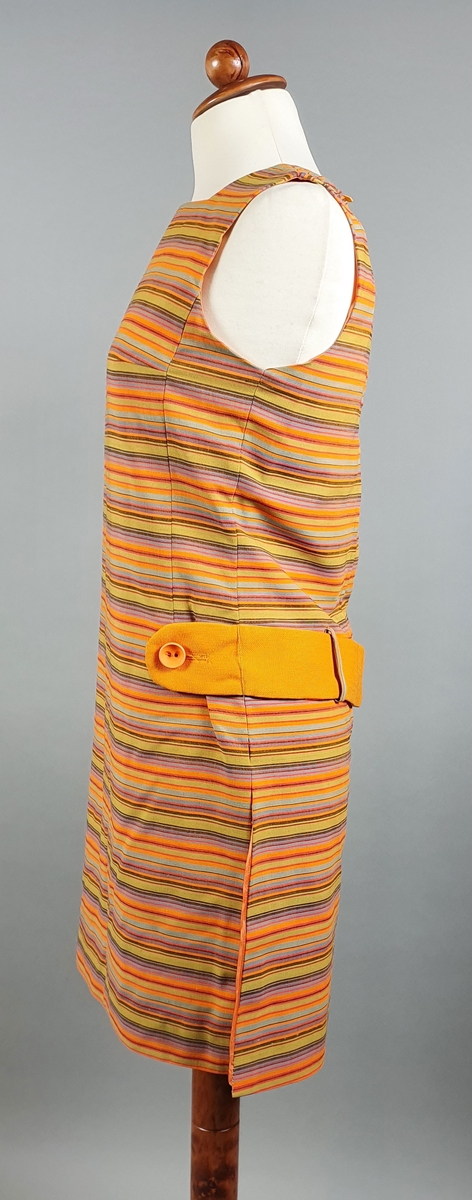 Tunika bestående av kjole og shorts (hotpants). Kjolen er uten ermer og har vertikale striper i oransje, grønt og brunt, med oransje belte (spensel) på ryggen med knapp som fester beltet på framsiden av hoften. Splitt i sidene.