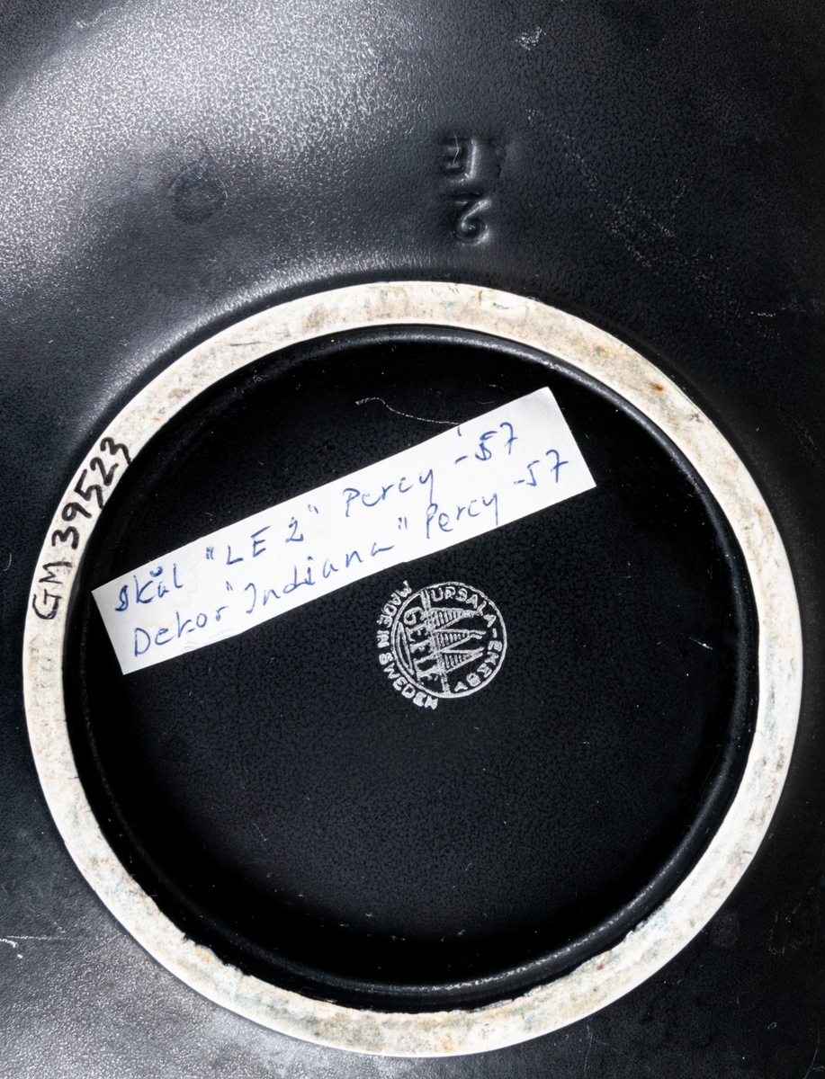 Större oval skål i flintgods med dekor Indiana i modell LE2, forrmgiven av Arthur Percy för Gefle porslin 1957. Insidan har turkos glasyr, utsidan har den matta svarta glasyren Negro. Längs skålens kant på insidan finns upphöjda dekorativa prickar i godset.