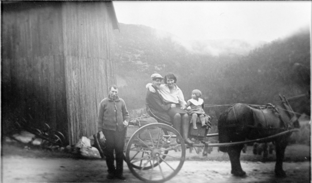 Hest og vogn, mann kvinne og barn i vogna.