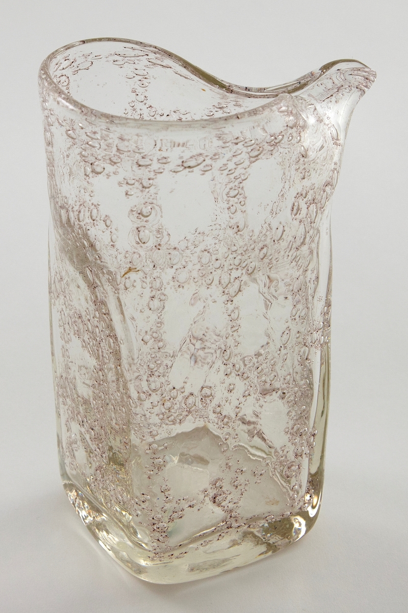 Mugge i klart glass med luftbobler. Boblene danner et rutemønster i glasset som følger muggens form. Vasens bunn er kvadratisk, mens øvre del er sirkulær. Ujevn formet munningsrand.