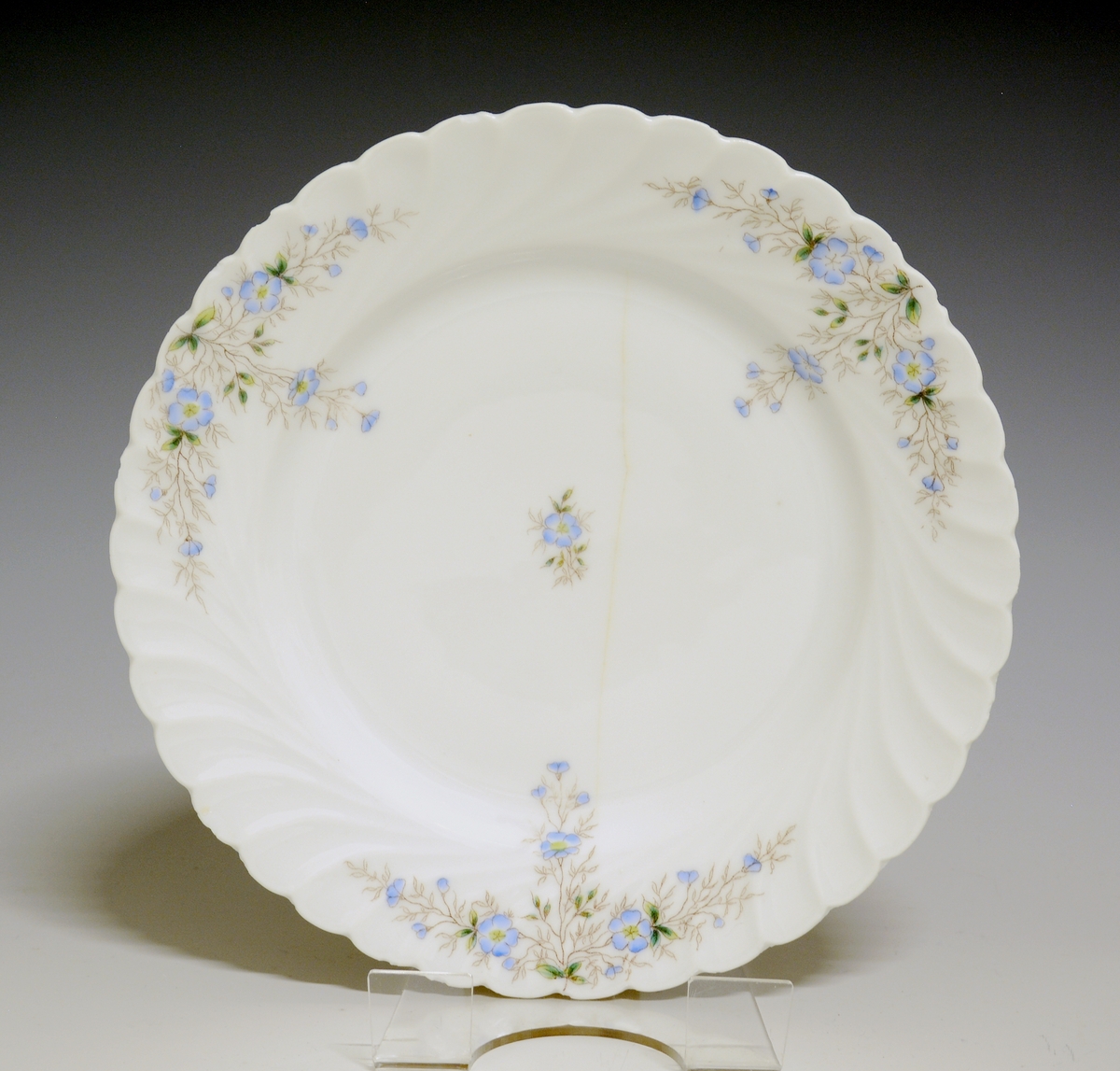 Flat desserttallerken av porselen med hvit glasur. Riflet gods, Dekorert med ståltrykkdekor med blå blomster. 
Modell: 1111.2 Tilhører Bordeservice 1111 (gammelt nr: 1112)
Dekornr: 1491
