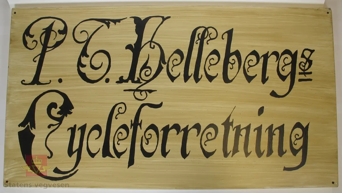 Rektangulært skilt lagd av metall, med teksten "P. T. Helleberg Cycleforretning" med svarte bokstaver på hvit/brun bakgrunn. Det er laget et hull i hvert av hjørnene.