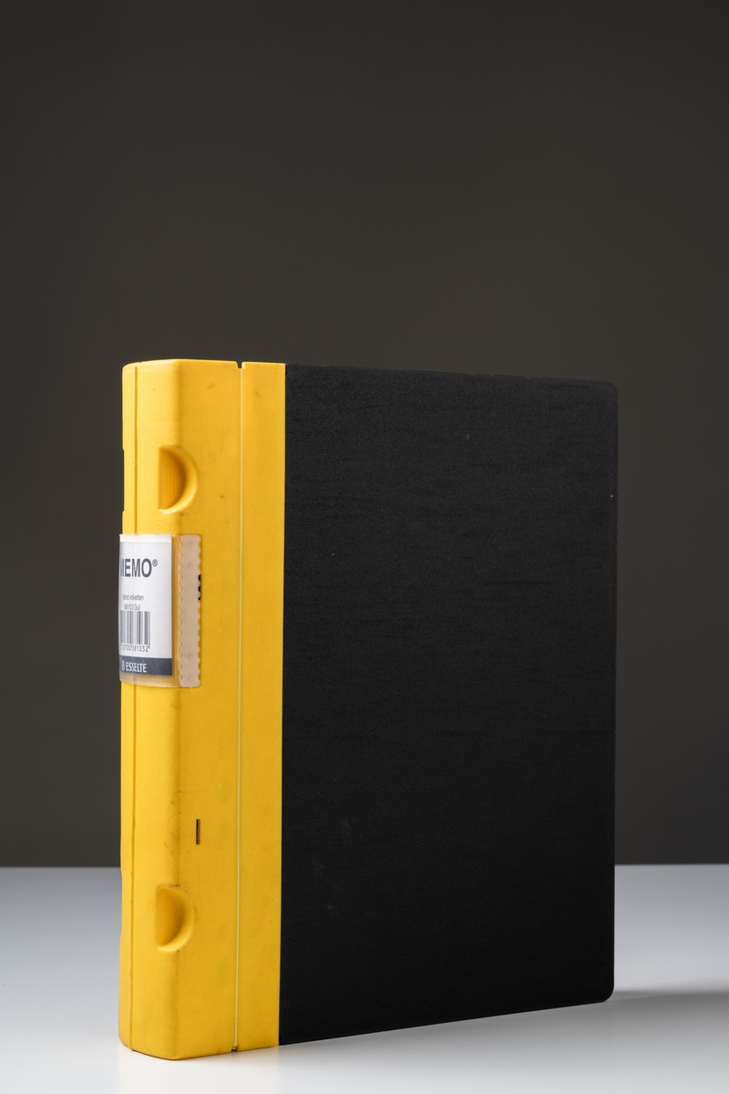 Pärm modell "MEMO" av gul plastrygg med svarta plastsidor. Pärmlås av metall. I ryggen gjutna grepp för fingrarna. Inuti pärmen står tryckt i relief "MEMO ESSELTE Made in Sweden".