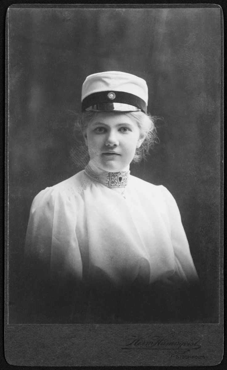 Visitkort, porträtt, bröstbild, föreställande ung flicka - Ellen Egnér - i vit blus, studentmössa och smycke, halslås av allmogetyp.