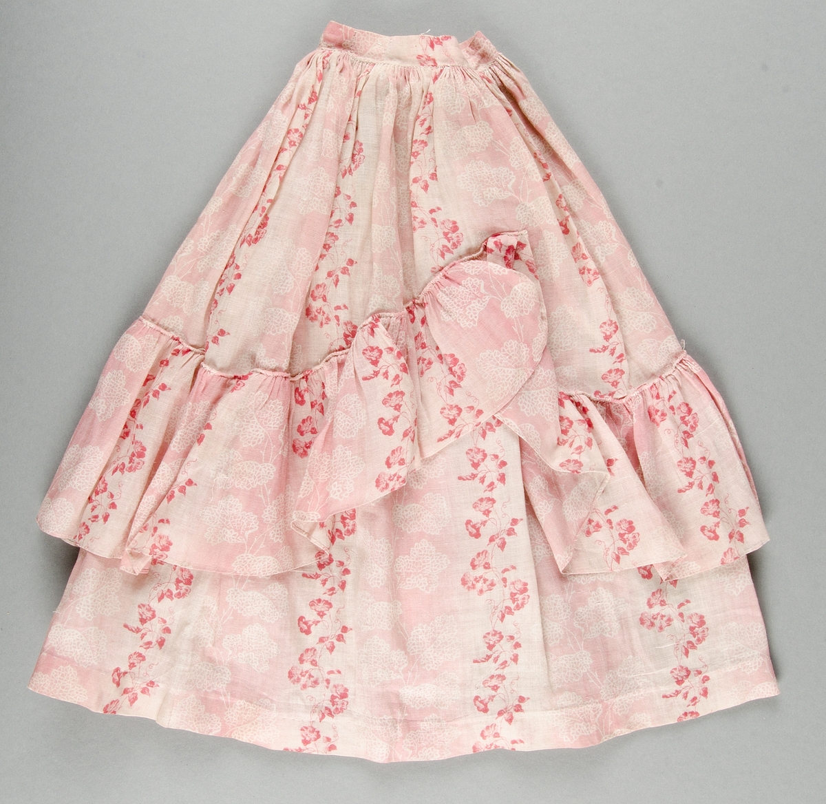 Blus och kjol av rosa- och vitrandig bomullsvoile med tryckt mönster i rött och rosa på vit botten. Livet kantat med röda ylleband.
