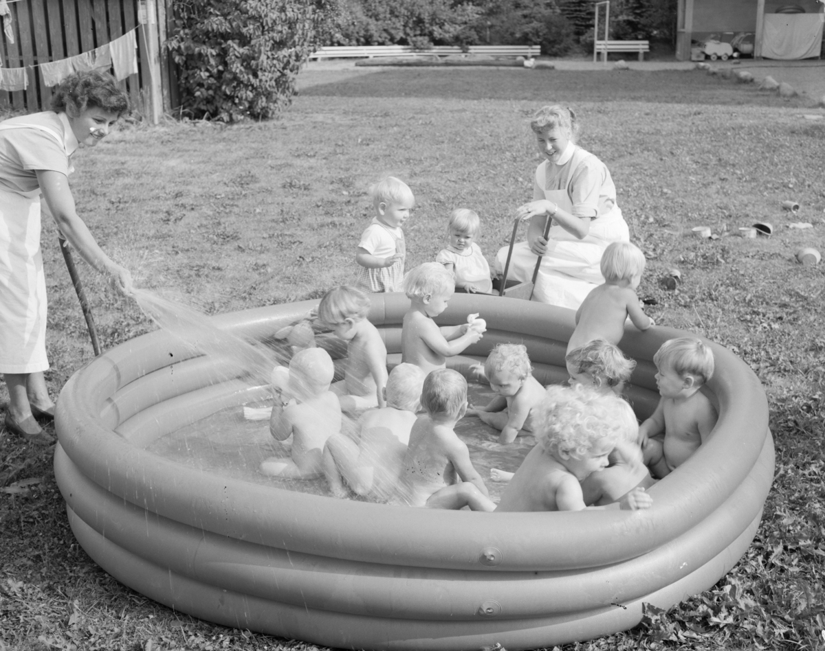 Fotografi av barn som leker i badebasseng og ansatte på Aline spebarnshjem.