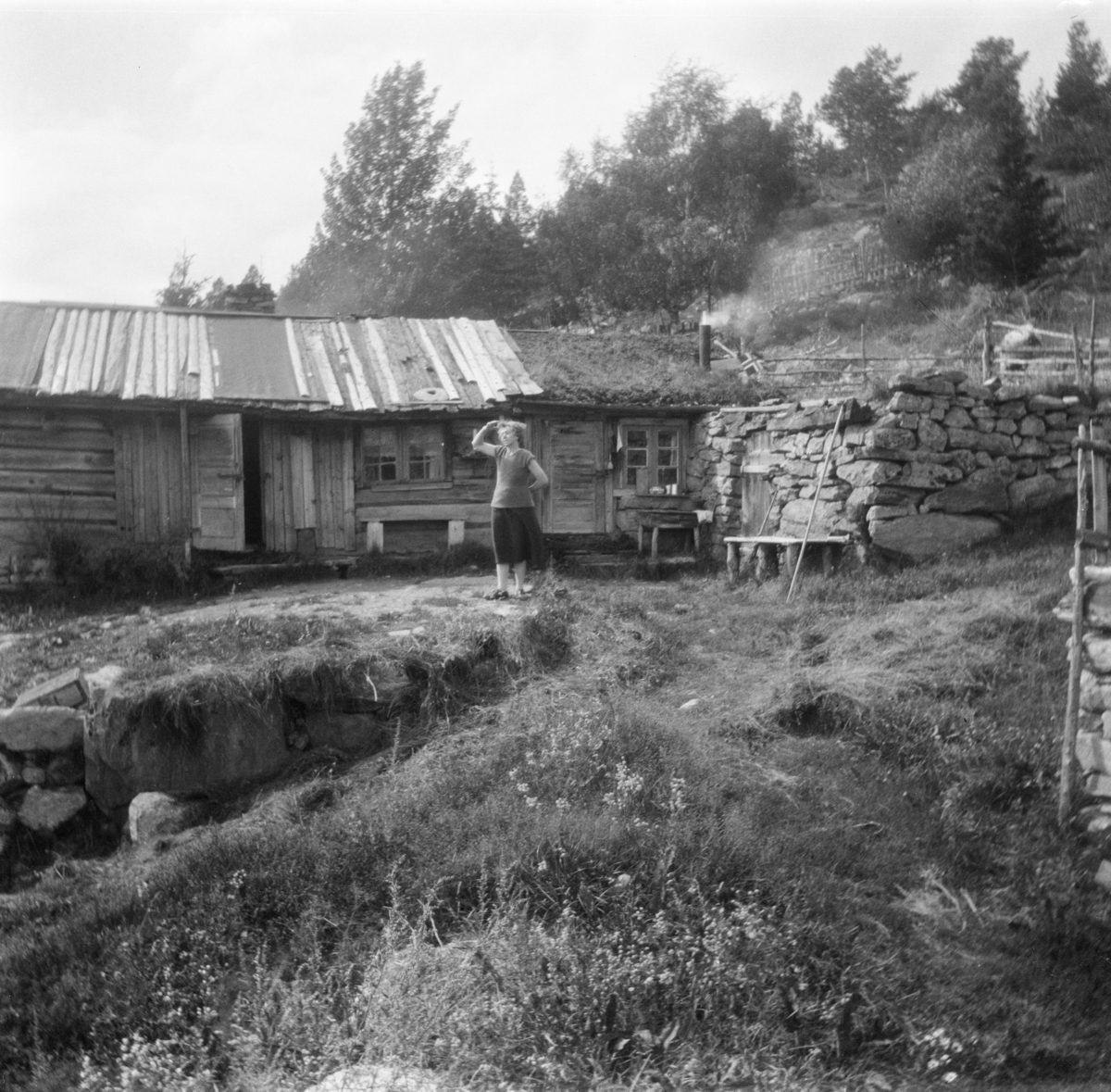 Kitty står foran gammelstugu og steinfjøsen i Haukdalen