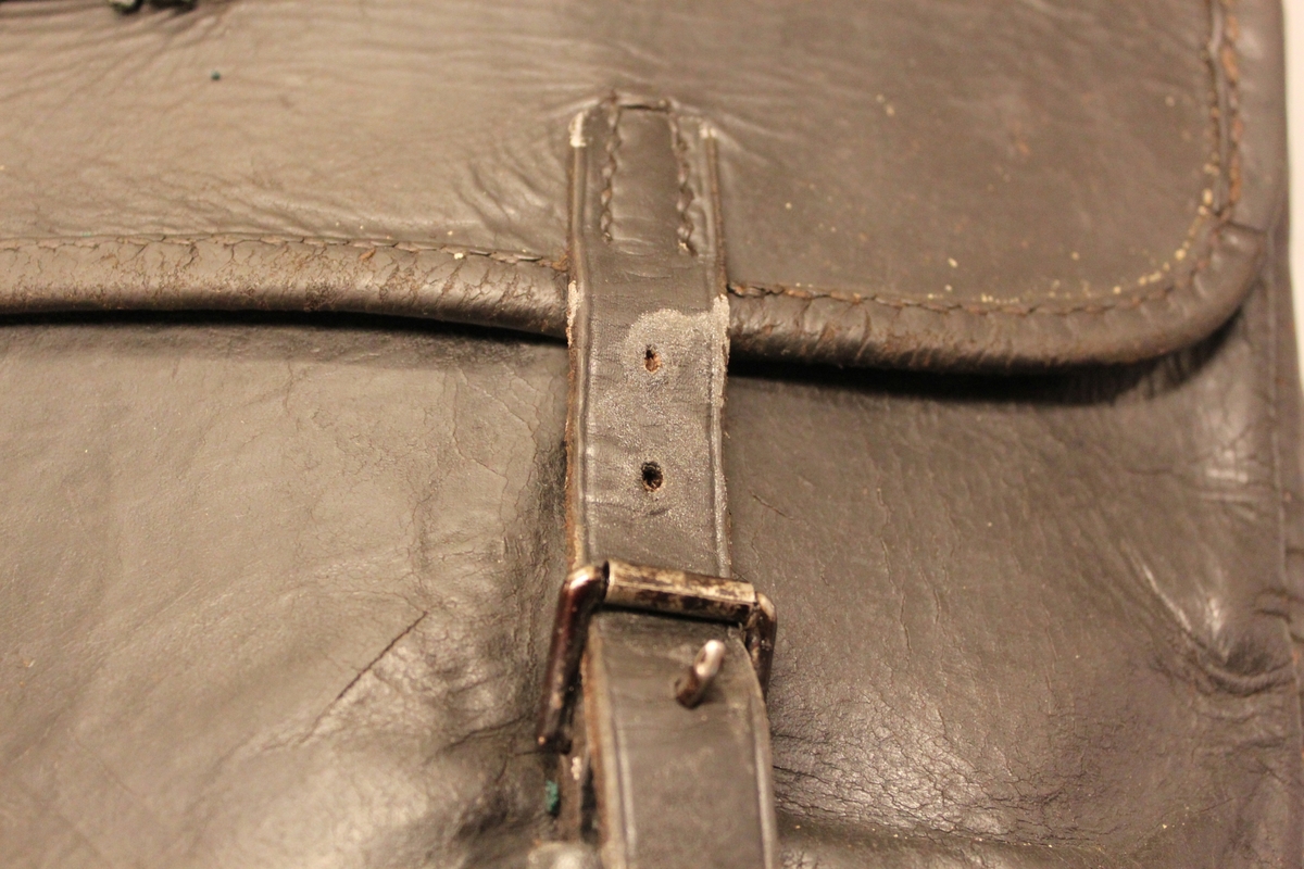 Väska av svärtat läder med klaff och två remmar och hålspännen. Låses med järnten (saknas). På klaffen en mässingsbricka märkt med "No 787".