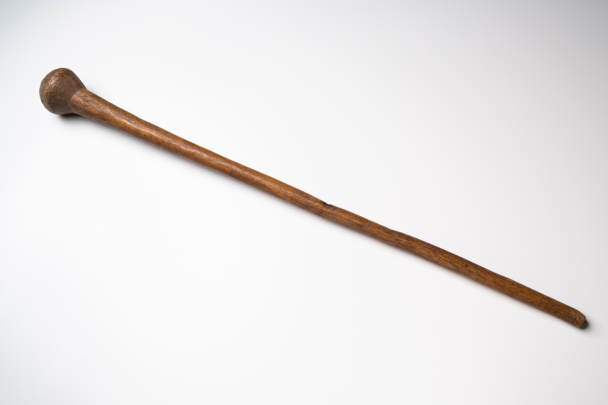 Mortelstöt av trä i form av en lång käpp med en klumpformad avslutning i ena änden.

Se vidare Historik.