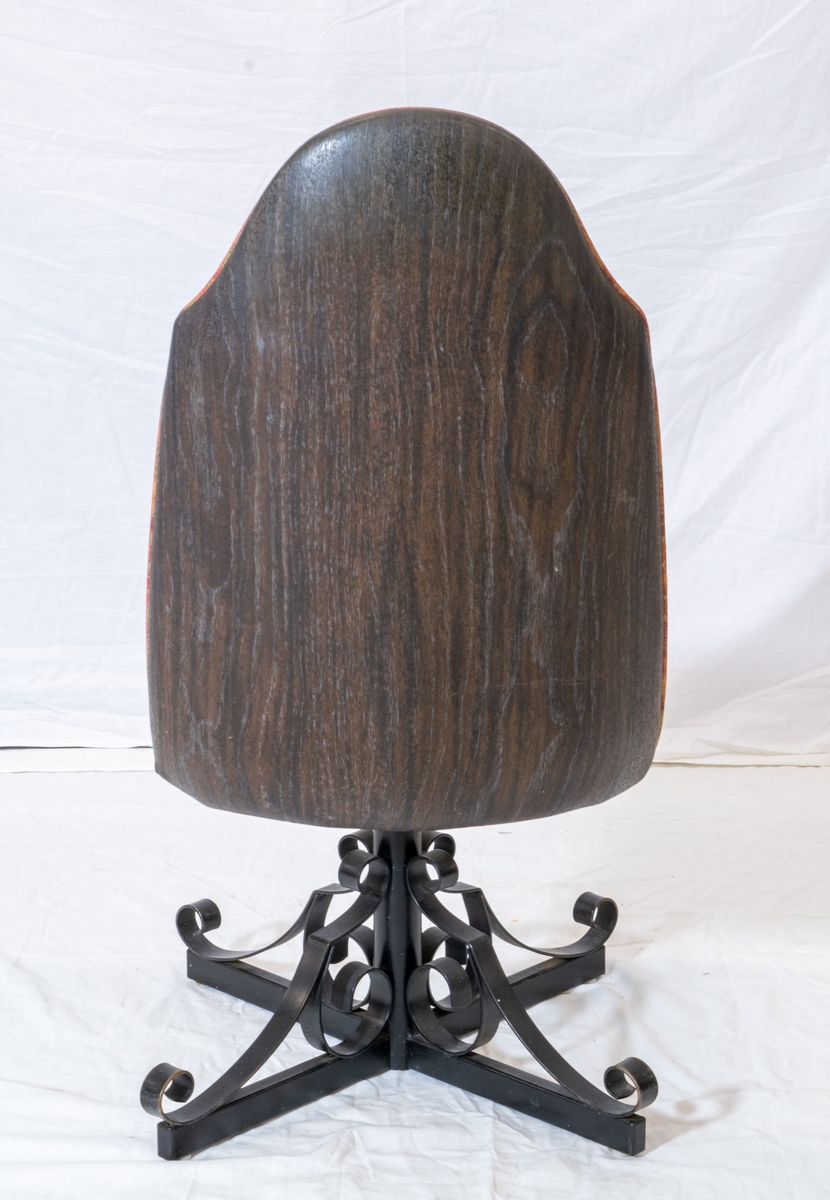 Spisestuestol med rødbrunt trekk. Bein i sort metall minner om smijern og bakplate i plast med tremønster.