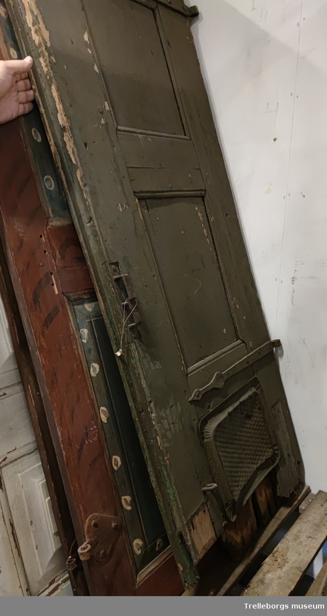 Dubbeldörr utan karm. Två dörrblad.
Målad dörr, mörkgrön, nästan svart.
Ena dörren kortare än andra. Båda dörrarna rejält slitna, nederkanten lägre på ena.
Ena dörren lagad med en metallbricka över hålet i nedre delen.
Oval rosett ovanför en rombisk spegel.