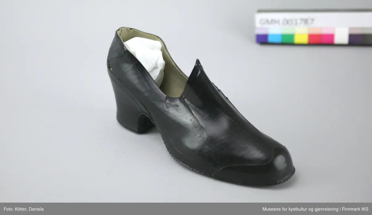 Denne kalosjen er en overtrekkssko av svart gummi. Den er foret med stoff og formen er egnet til damesko med høyere hæl.
