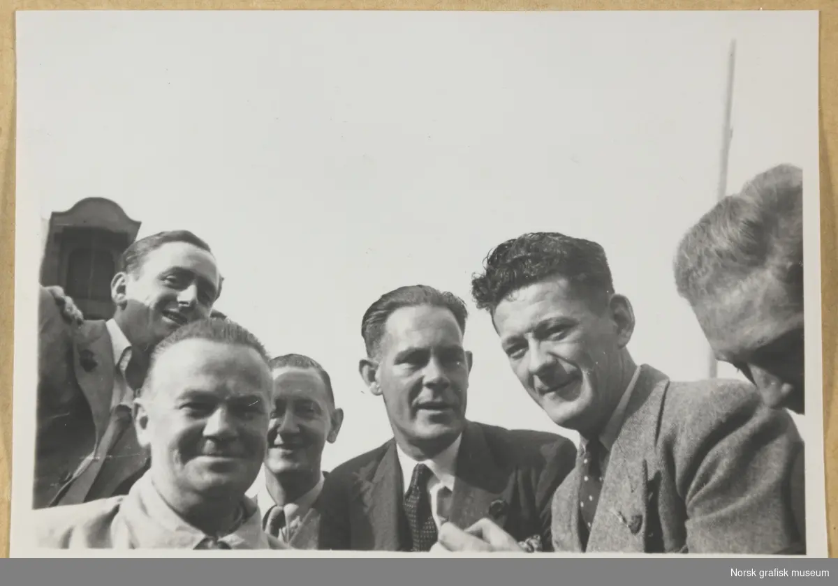 Gruppebilde, utendørs. Halvnært utsnitt av seks smilende menn i dress og slips. Fotografert i forbindelse med Vestlandsk Trykkerstevne i Bergen, 1946.