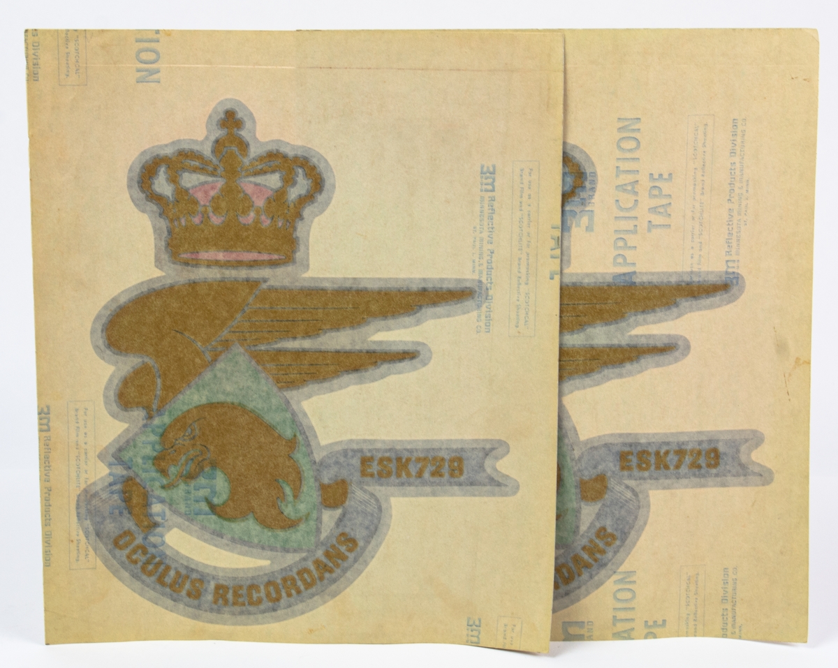 Klistermärken till dansk dekal, en utbildningsgåva från Eskadrillen 729. Märkena visar en vapensköld, den danska kungakronan, ett vingpar och ett baner. ESK 729 OCULUS RECORDANS APPLICATION TAPE.