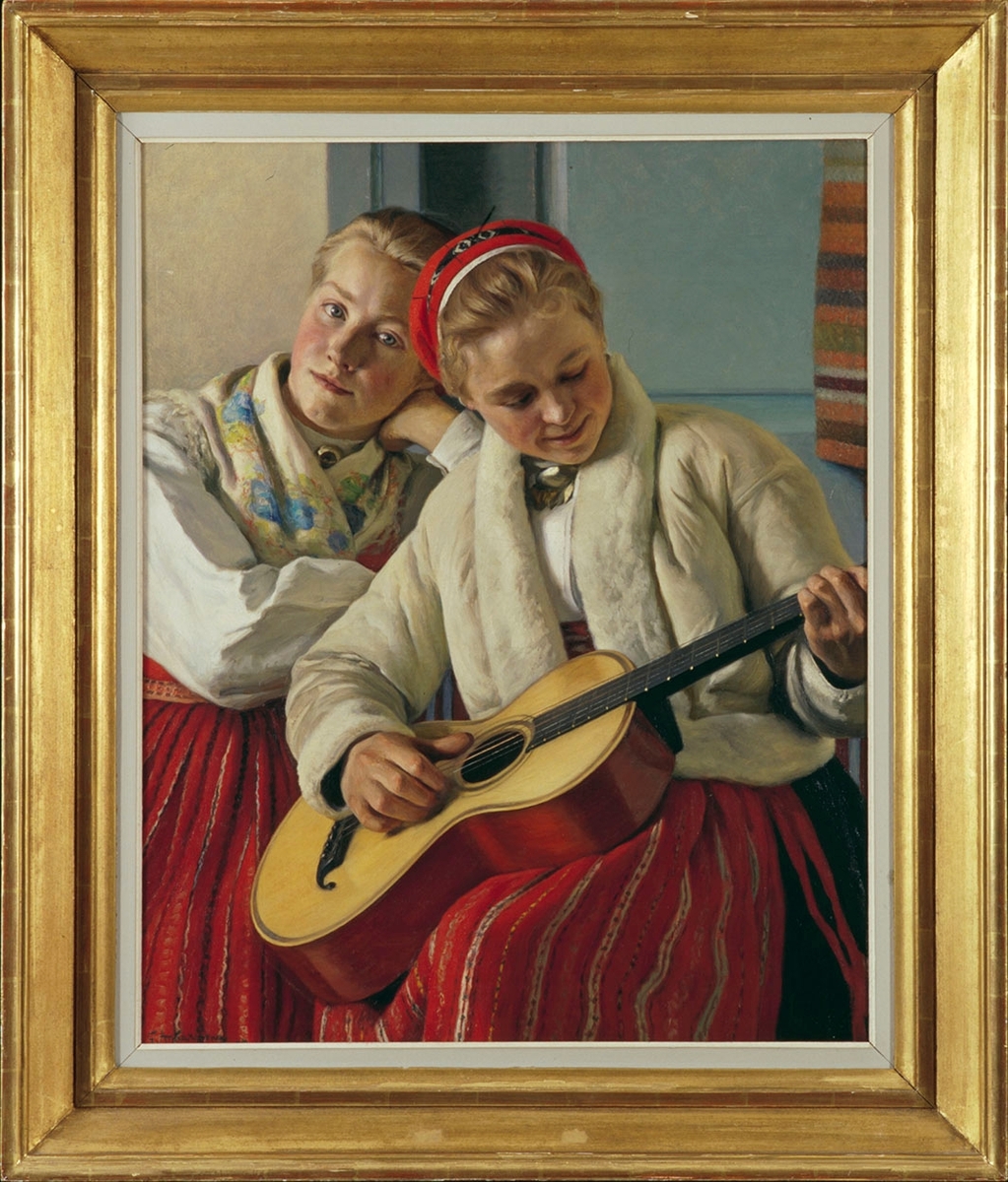 Två unga kvinnor i Leksandsdräkt sitter intill varandra mot ljusblå bakgrund. Den ena spelar gitarr och bär skinntröja. Båda bär det vanliga rödrandiga förklädet, den sk rödmajden, som är ett av Leksandsdräktens många förkläden.