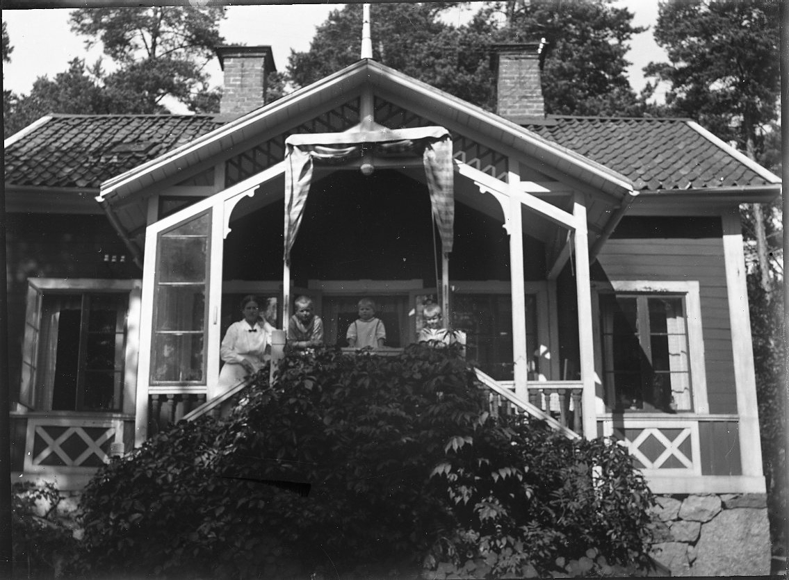 En kvinna och tre barn kikar ut från en delvis glasad veranda.