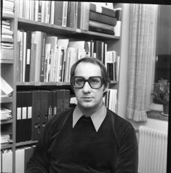 En skolman med glasögon sitter framför en bokhylla med böcke