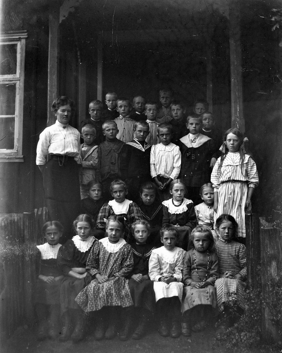 Elever samlade med lärarinnan på skolans farstukvist. Pojkarna står upptill och flickorna, utom en, sitter ned framtill.