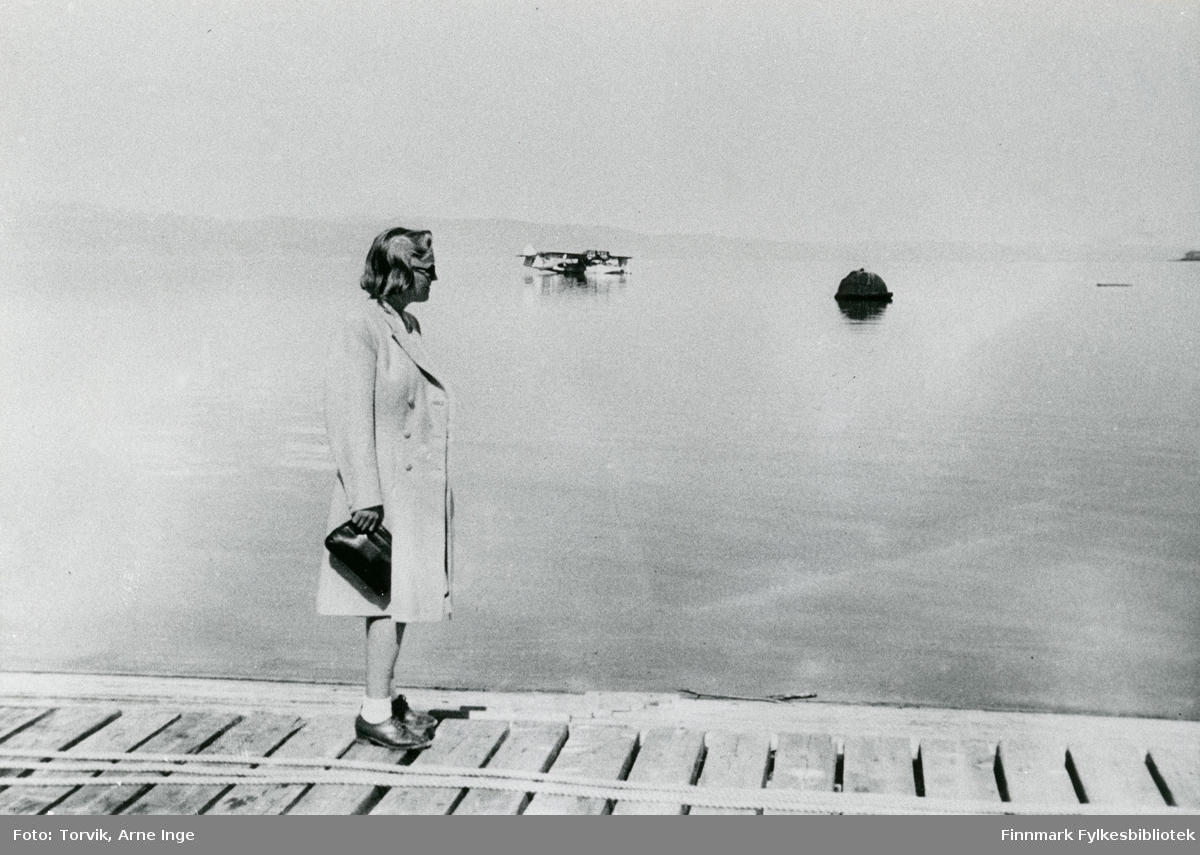 En ukjent dame står på dampskipskaia i Vadsø havn i 1947. I bakgrunnen ser vi et sjøfly. På den tiden var det havnebassenget som var flyplassen i Vadsø.