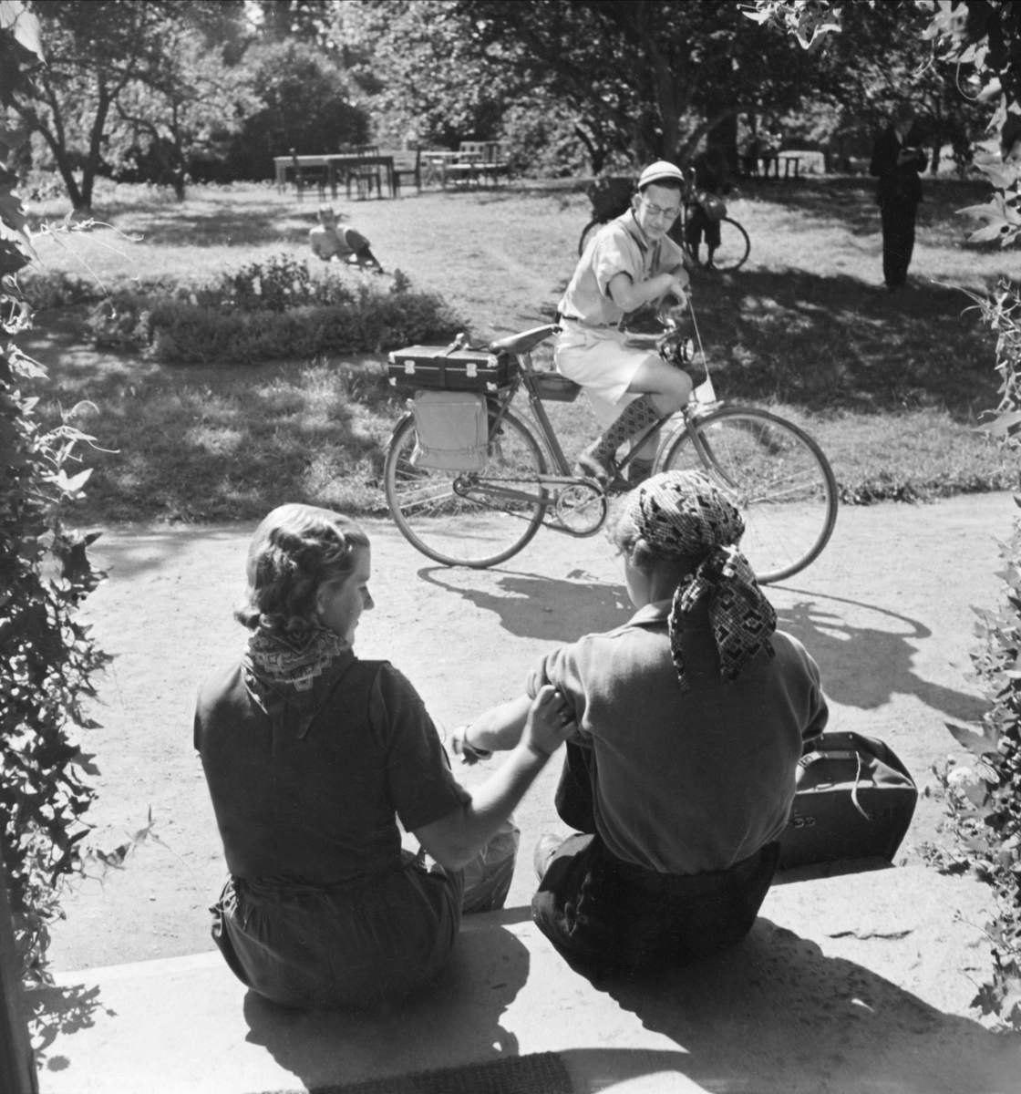 Ungdomar vilar under cykelfärd. Två flckor sitter på en trappa, en ung man står med cykel på vägen framför dem.