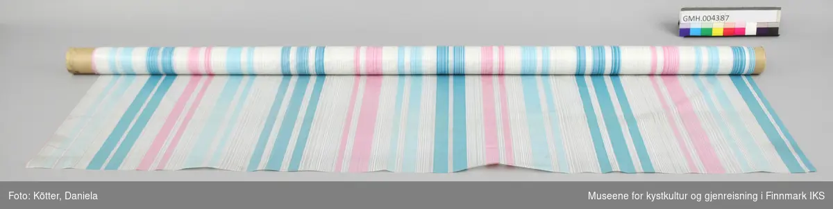 Duken er av kunststoff, er delvis gjennomsiktig og har hvite, lyseblåe, blåe og rosa striper. Den er rullet på en pappkjerne som har et påskrift fra utsalgsstedet. 