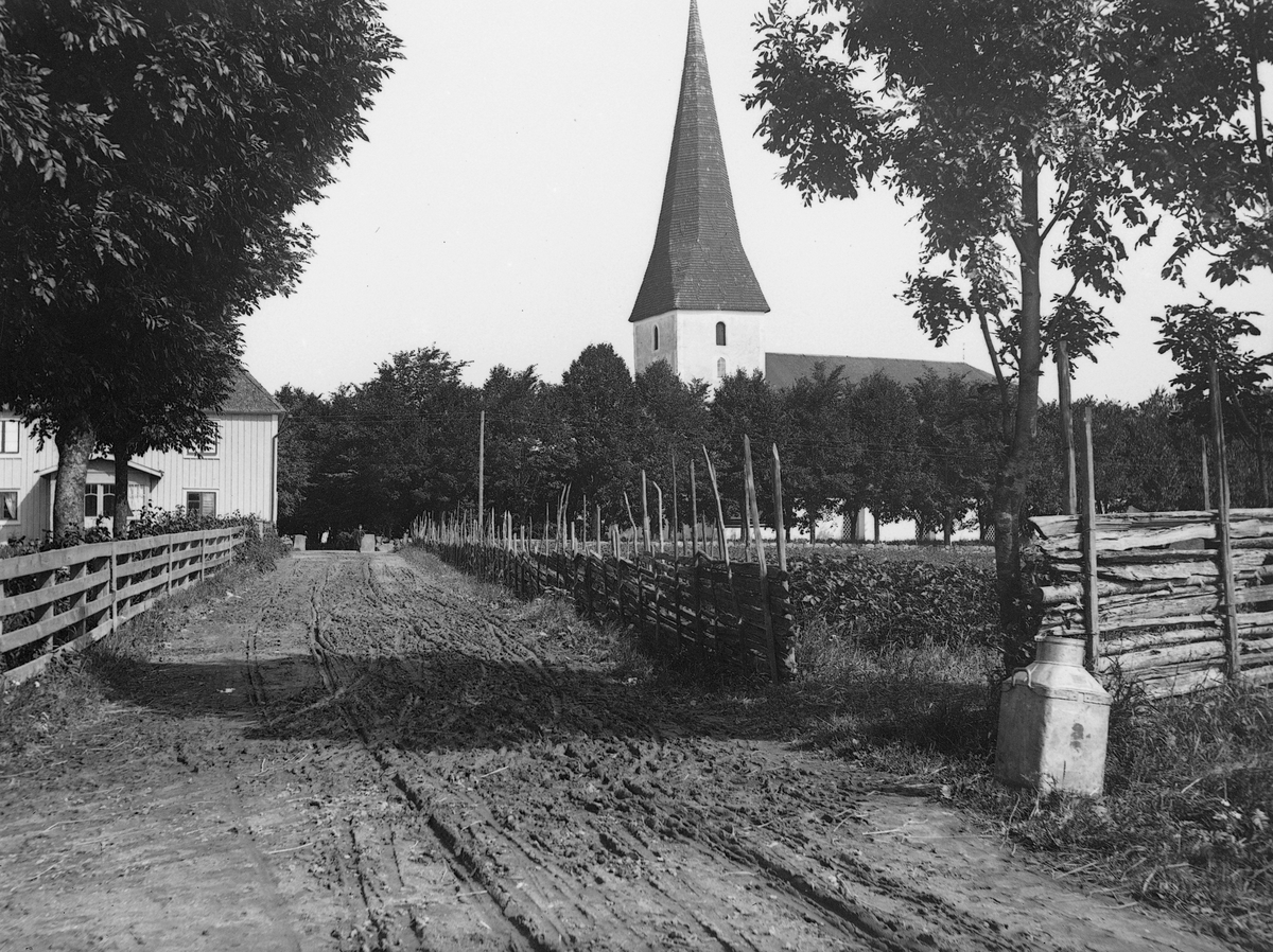 Vy längs vägen genom Viby omkring 1905. Till vänster Källgården med ortens handelsbod, som vid tiden upplysningsvis drevs av bildens fotograf, Carl Sundström. Till höger församlingens kyrka som stått på platsen sedan 1100-talet.