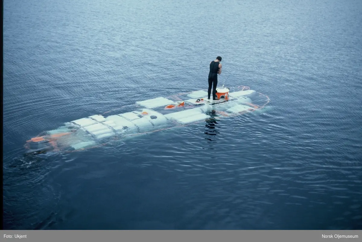 En ubåt løftes fra en lektert og ut i sjøen. En mann i våtdrakt står oppå ubåten under hele løftet.