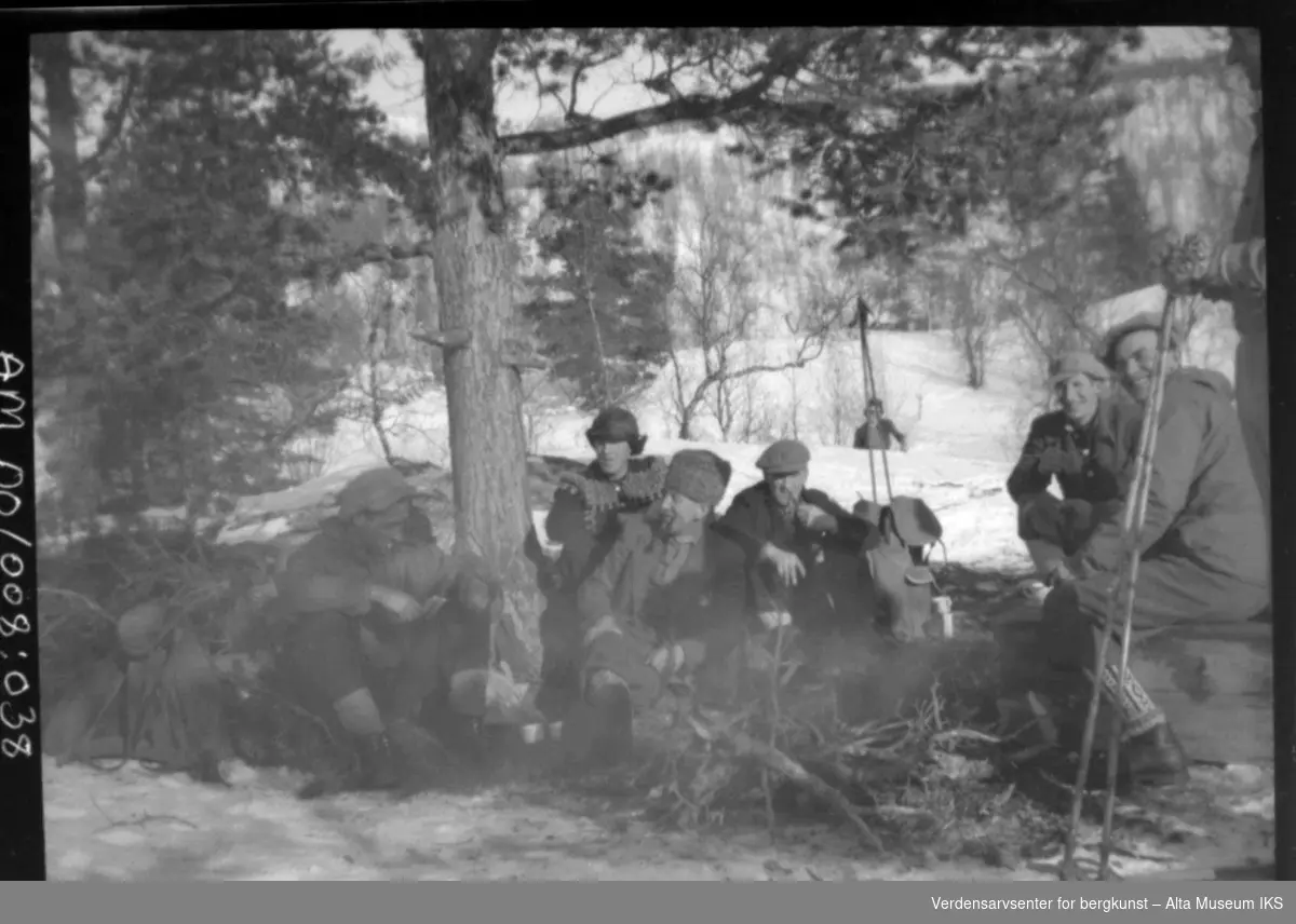 Gruppe menn på skitur koser seg med bål i skogen under et tre.