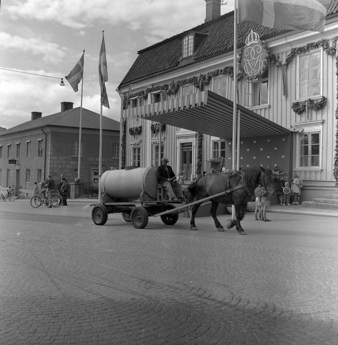 Utanför Rådhuset har man förberett inför  Gustav VI Adolfs besök. En man med häst och vagn kör en vattentank för spolning av gatorna.
