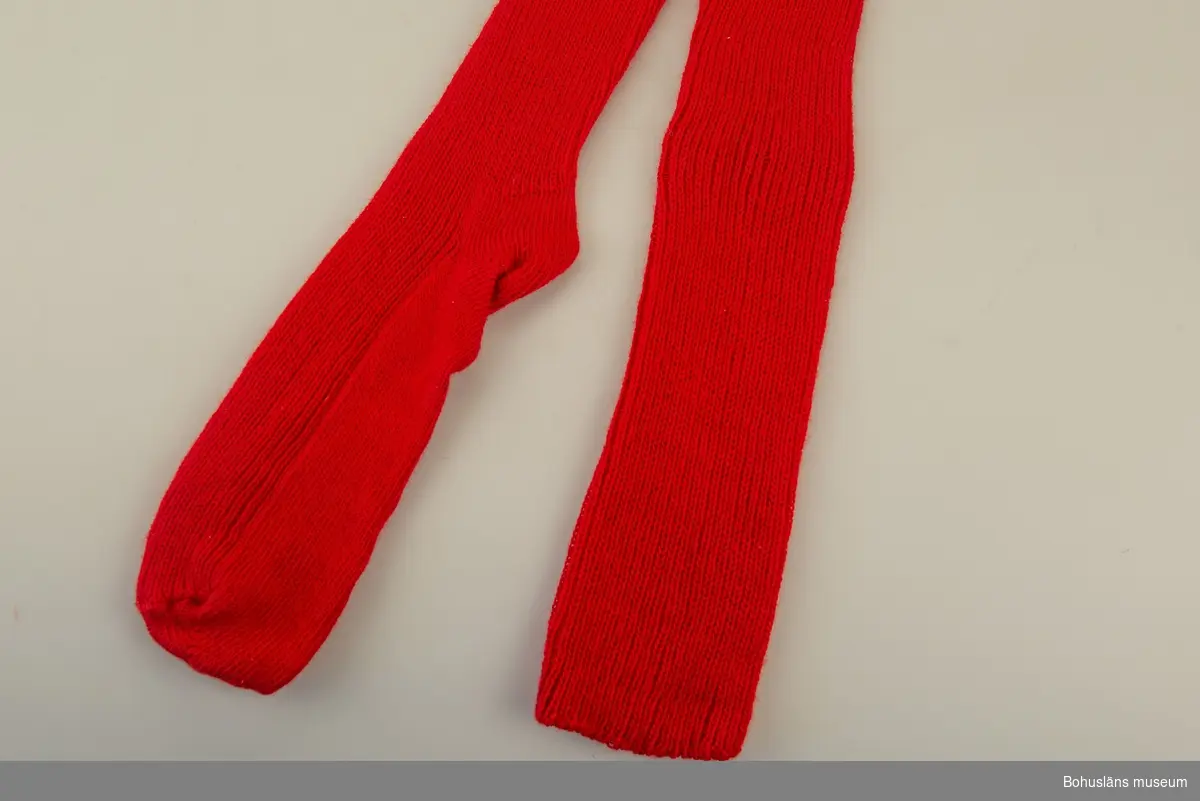 Del av bohusdräkt.
Enfärgad resårstickad röd strumpa handstickad av ullgarn, slätstickning under foten. 
För att hålla strumpan på plats ska möjligen ett strumpeband knytas över knäet.
Samhör med UM033951.