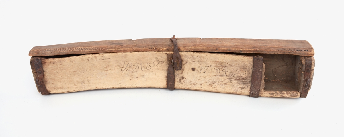 Liefodral, trä, beslag av järn, tre stycken, löper runt fodralet, de två i ändarna försedda med öglor för att kunna transporteras,. Svagt bågböjt, urholkat ur ett stycke, försedd med hasp och lock längst ena långsidan. Locket varit fastsatt med små järnbeslag (spår av detta i träet). På ovansidan ristat i träet:
"L M S" med dekorativa ornament, till vänster om järnhaspen.
"1734" till höger om järnhaspen.