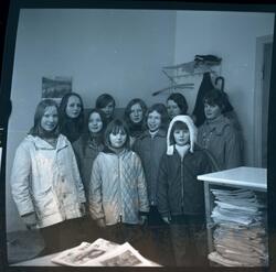 Fotografi av ti jenter kledd i vinterklær som står i et rom 