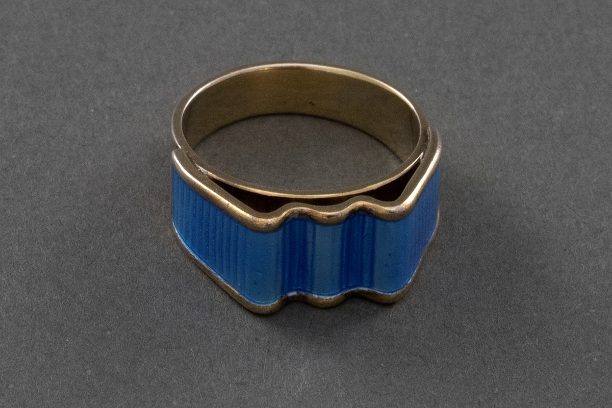 Forgylt sølvring med en bølgeformet topp og lyseblå speilemalje. Toppen og ringen er utformet hver for seg og så sveiset sammen.