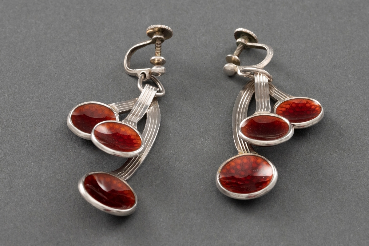 To kirsebærformede øresmykker i sterling sølv med rød speilemalje. Hvert smykke er formet som tre kirsebær som knyttes sammen i roten på stilken.
