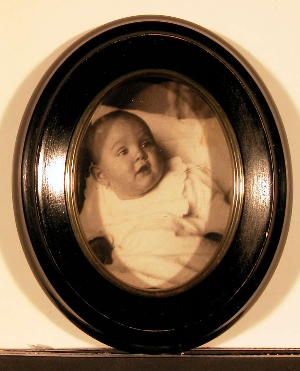 Babyportrett; piken liggende støttet opp av puter.