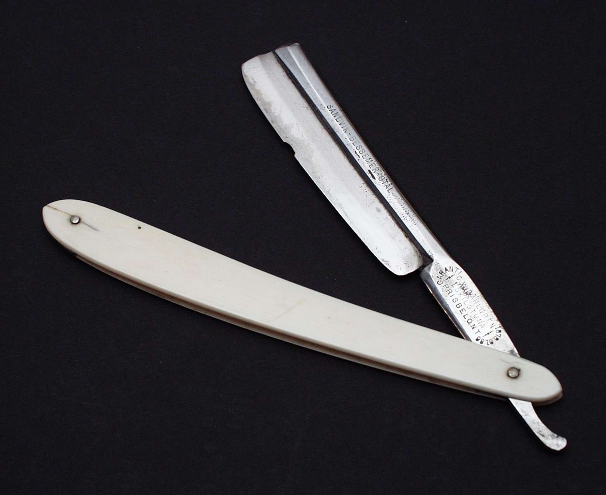 Barberkniv i stål med buet hvitt treskaft. Kniven er sammenleggbar.