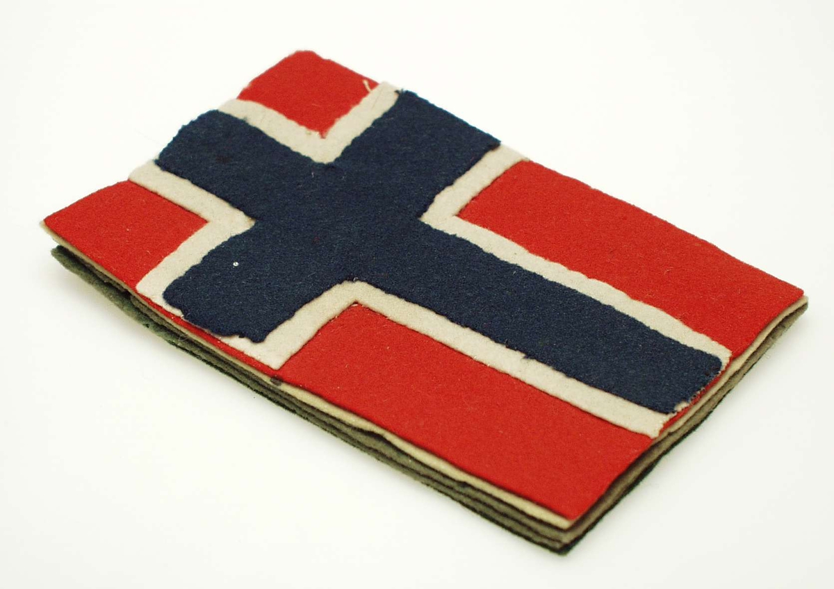 Pennetørker av flere lag filt formet som det norske flagget. Lagene er sydd sammen med fem sting ved flaggkorstet.