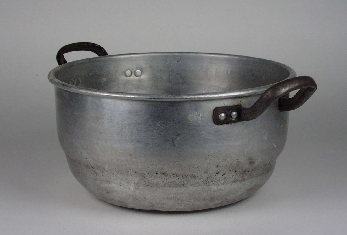 Kjele i aluminium med påklinkede hanker. Den har vært brukt på vedkomfyr.