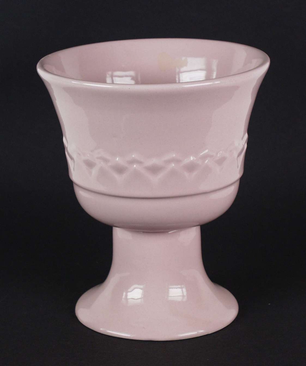 Rosa potteskjuler formet som en pokal. Den er i keramikk og har en bord i godset.