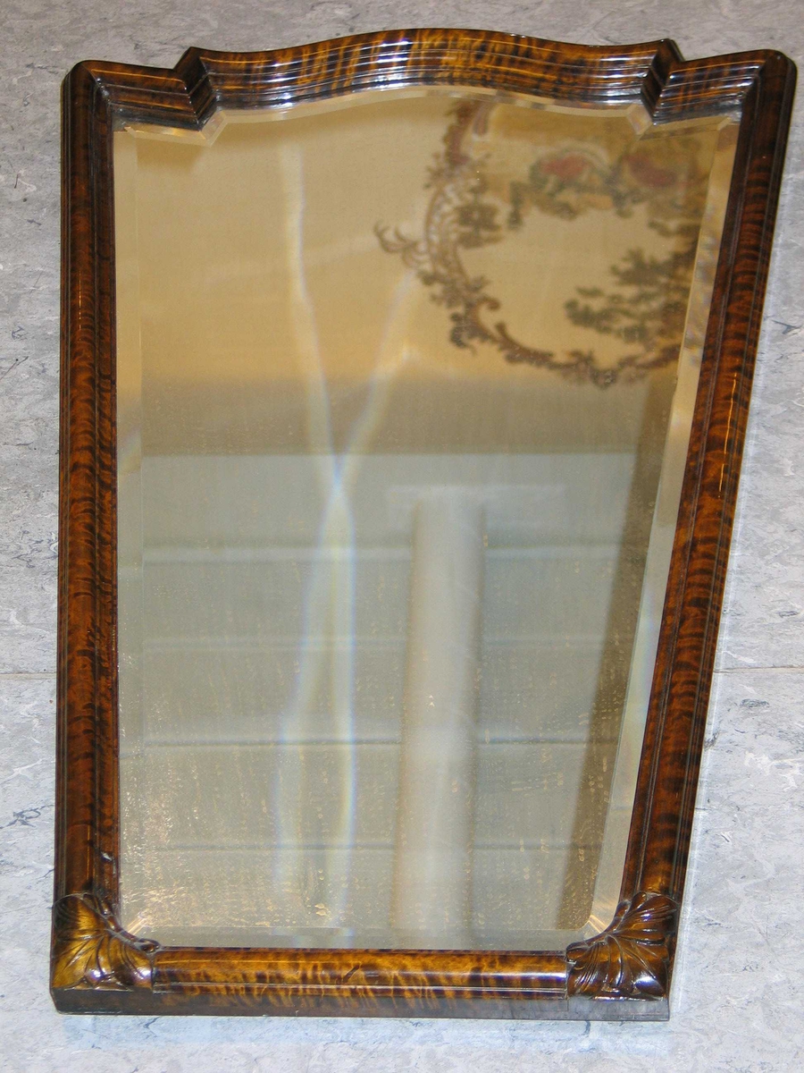 Trapesformet speil med ramme i tre. Speilet har en bred slepet kant. 