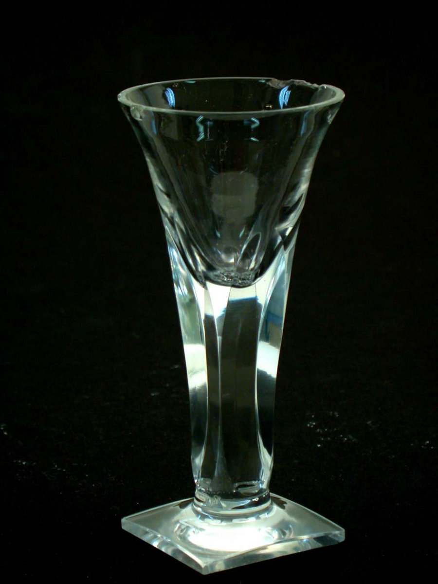 Glasset er et spissglass med firkantet fot. Stetten er fasettslipt slik at den blir firkantet. Det er flere hakk i randen på klokken. 