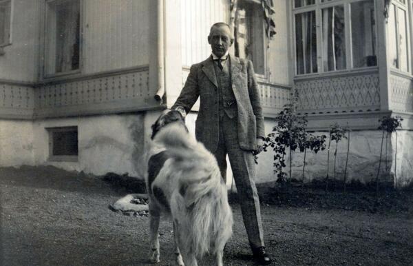 Mann står sammen med en hund foran hus.. Foto/Photo